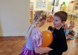 chłopiec i dziewczynka przebrani w stroje karnawałowe tańczą z balonem