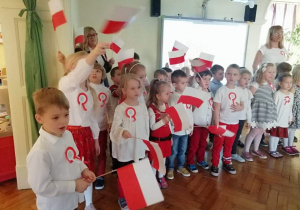 dzieci ubrane na galowo trzymają chorągiewki biało-czerwone w ręku