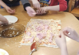 dzieci siedzą przy stole i robią pizze