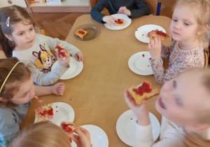 dzieci siedzą przy stole i jedzą pizzą