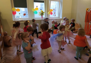 Kilkanaścioro dzieci w jesiennych strojach tańczy swobodnie.