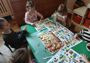 Dzieci układają składniki na pizzę a dziewczynka trze ser