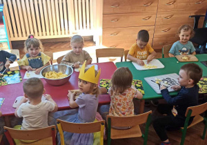 Dzieci z grupy 1 siedzą przy stolikach i kroją jabłka na ciasto