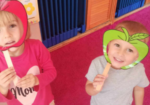 Dziewczynka i chłopiec pozują do zdjęcia w jabłkowych maskach