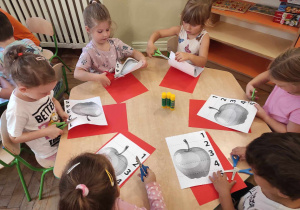 Dzieci z gr 2 siedzą przy stolikach i wycinają puzzle jabłkowe