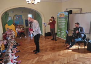 Pan Maciej śpiewa piosenkę, Pan Krzysztof gra na puzonie, Pan Michał gra na harmonii a dzieci słuchają