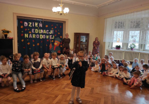 Dziewczynka z gr 4 mówiąca wierszyk na tle dzieci z naszego przedszkola