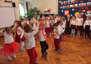 Dzieci z grupy 3 tańcący do muzyki z białymi i czerwonymi wstążkami