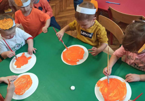 Dzieci z grupy 1 przy stolikach kolorują talerzyki plastikowe