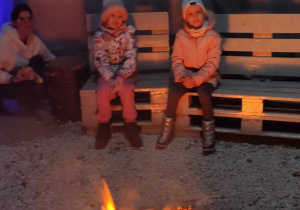 Dziewczynka z grupy 4 i dziewczynka z grupy 5 siedzą przy ognisku