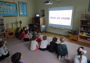 Dzieci z grupy 2 oglądają film edukacyjny o kotach na tablicy multimedialnej