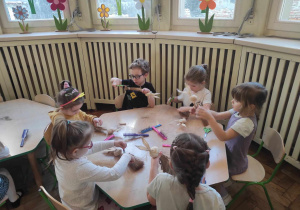 Dzieci przy stolikach odcinają nożyczkami zbędne sznurki
