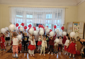 Grupa maluszków i 2 grupy średniaków śpiewają hymn trzymając balony