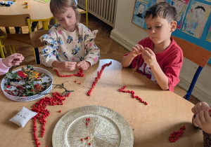 dzieci siedzą przy stole, nawlekaja jarzębinę na sznurek